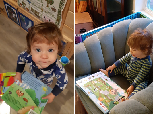 Toddler holding book looking at camera next to toddler in chair reading book